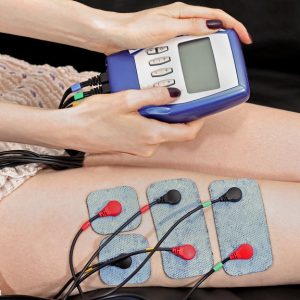 Woman sitting on medical table while wearing an eletrostimulation unit on her thighs.