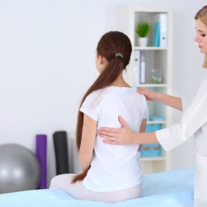 Female chiropractor evaluating young female patient's back for scoliosis.