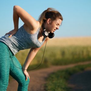 Woman holding lower back in pain while out running on a trail.