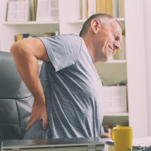 Man sitting in a computer chair and holding his lower back in pain.