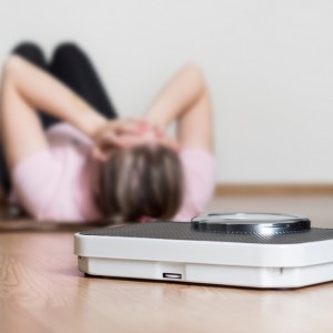 Image of a scale with a person in the background on the ground, upset about their weight